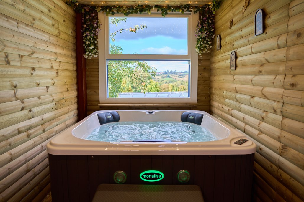Private hot tub at The Lórien Spa, Laneside Holidays, overlooking the Esk Valley through a large window, with floral decorations and fairy lights.